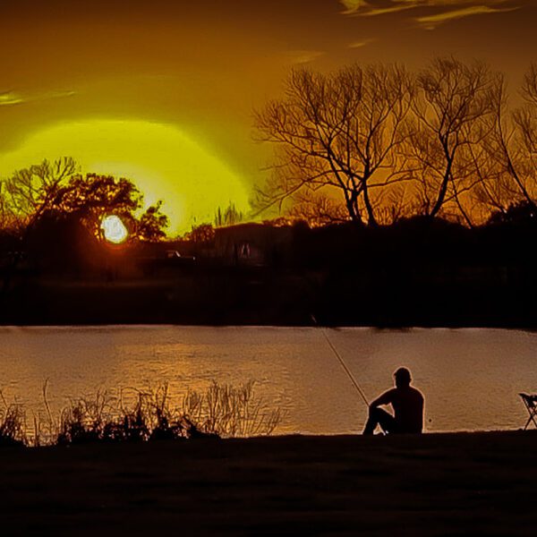 A person sitting on a bench watching the Austin set over a lake.