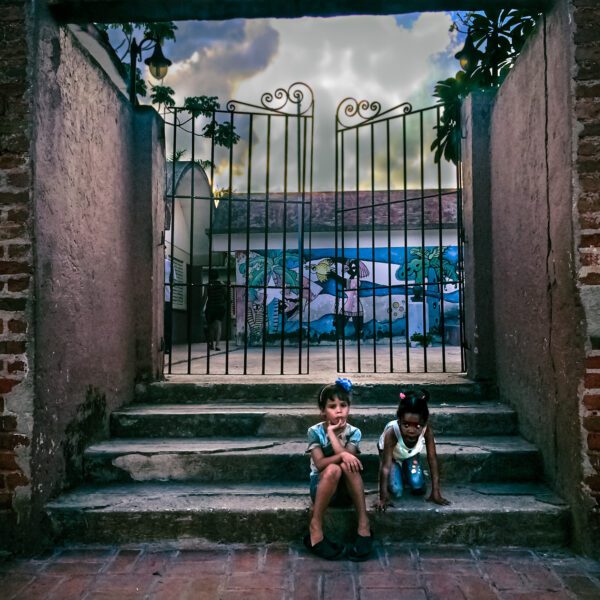 Two children sitting on steps in front of a Cuba gate.