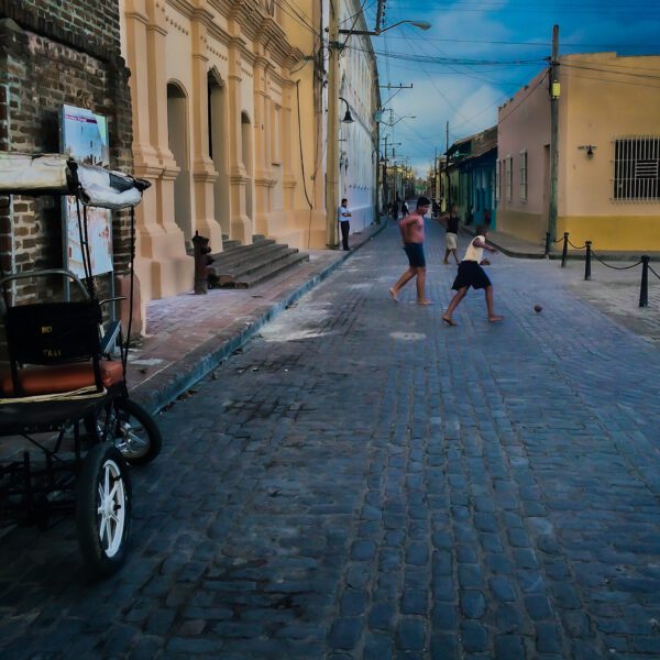 A street scene with a Cuba and people walking down a cobblestone street.