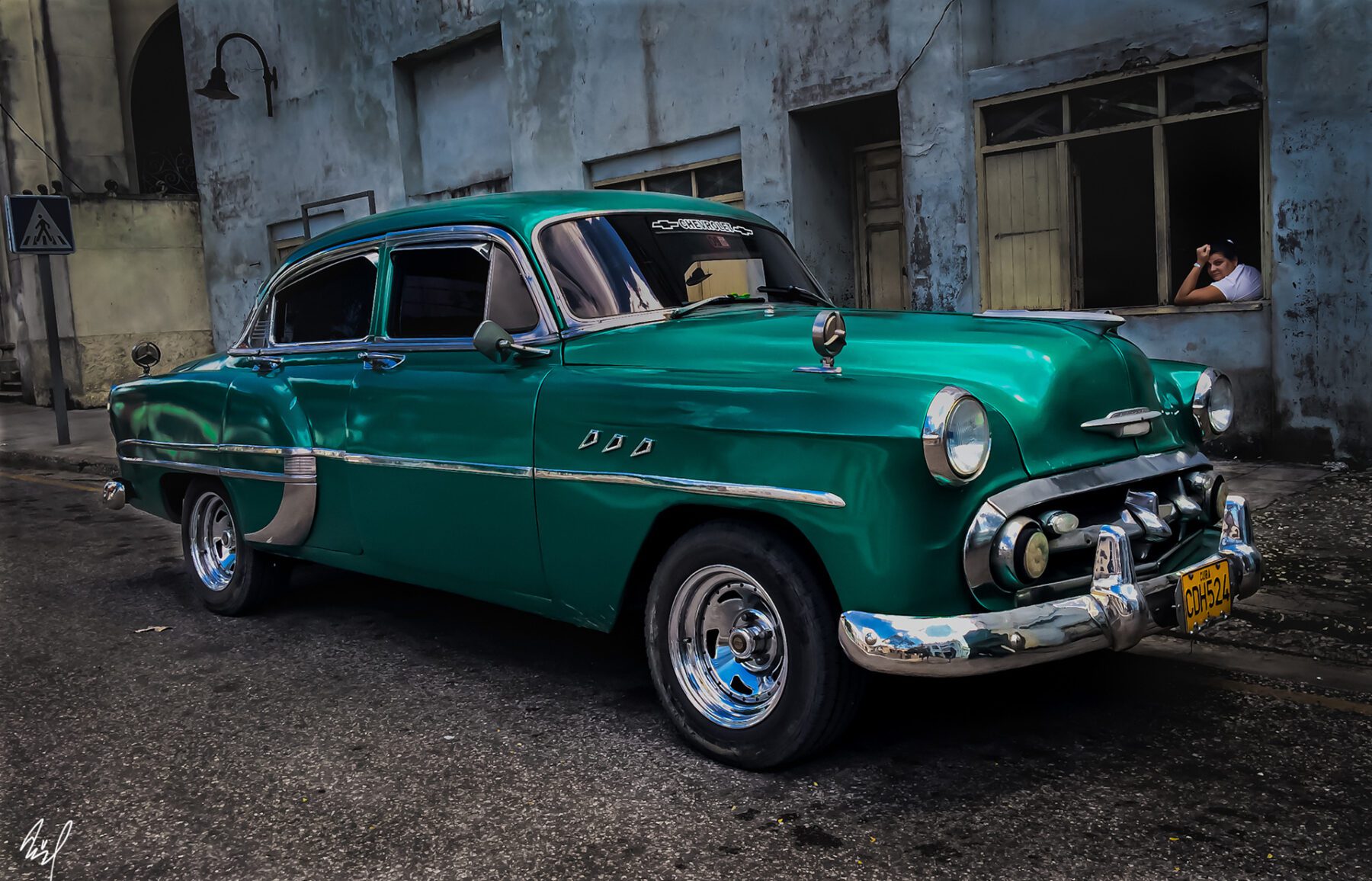 An old green Cuba is parked in front of a building.