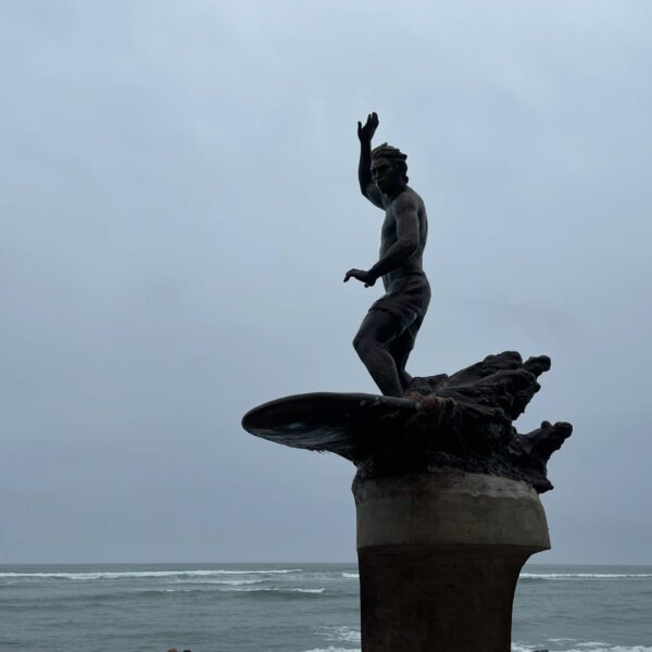 A statue of a surfer standing on top of a Peru surfboard.