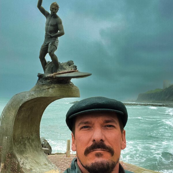 A man is taking a selfie in front of a statue of Peru.
