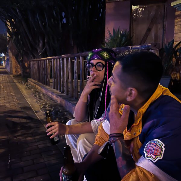 Two men sitting on a sidewalk drinking Peru.