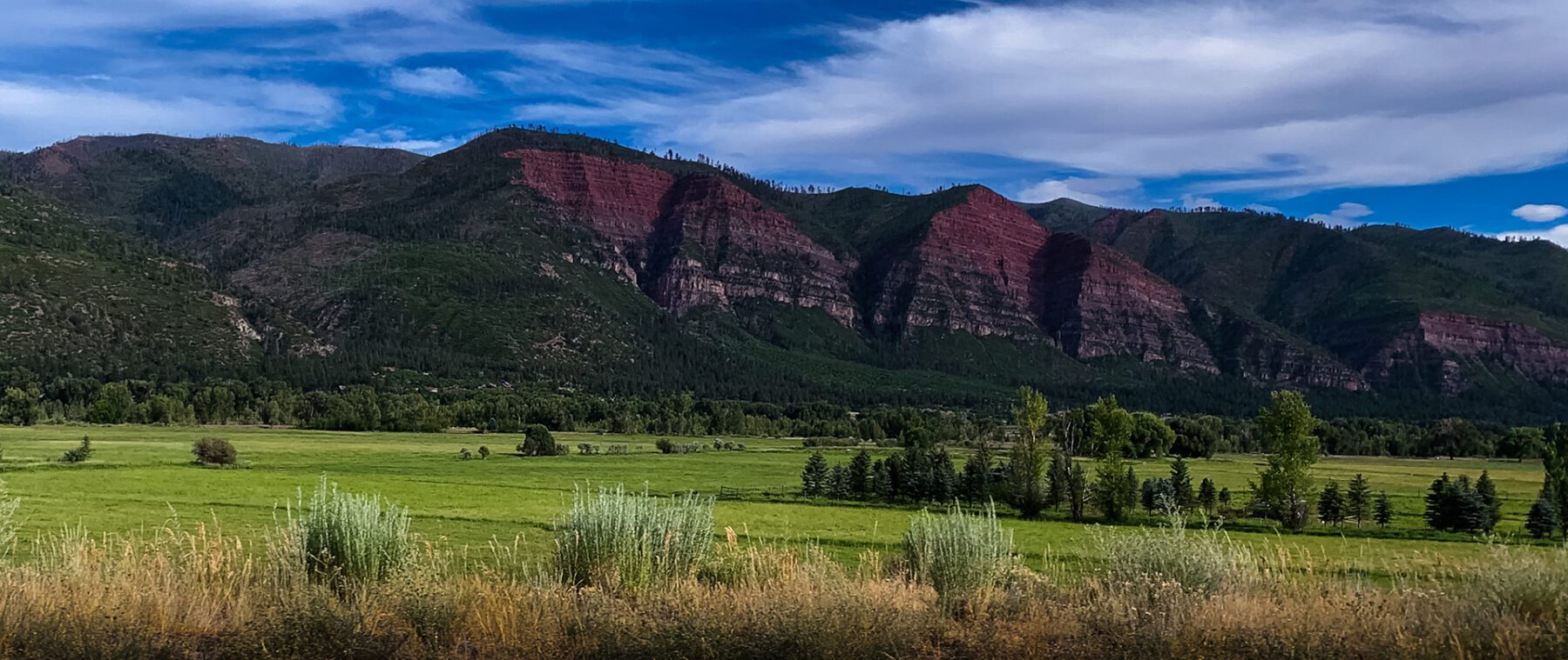 A red mountain range with grass and trees in the background.