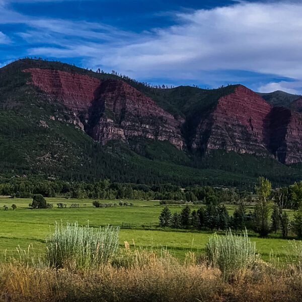 A red mountain range with grass and trees in the background.